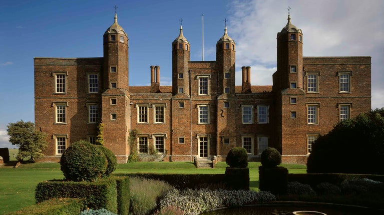 The West Front of Melford Hall, a red brick house showing 4 towers and ogee roof